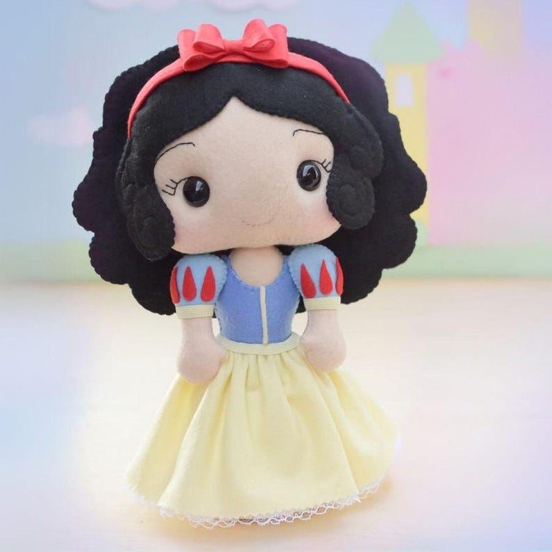 May include: A handmade Snow White doll with black hair, a red headband, and a yellow dress. The doll has a blue bodice with red and white sleeves. The doll is made of felt and has large, expressive eyes.