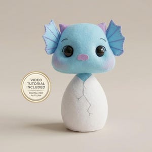 May include: A handmade blue felt creature with large black eyes, purple accents, and wing-like ears, emerging from a white felt egg. The image includes a circular graphic with the text "VIDEO TUTORIAL INCLUDED" and "DIGITAL PDF PATTERN".