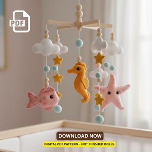 Può includere: Mobile per bambini fatto a mano con creature marine in feltro: un pesce rosa, un cavalluccio marino arancione e una stella marina rosa. Il mobile include anche nuvole bianche, stelle gialle e perline blu. Il testo "DOWNLOAD NOW" è visibile.