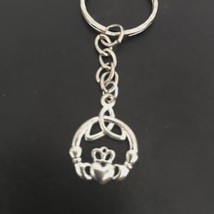 May include: Silver-colored Claddagh keychain. The Claddagh design features a heart, crown, and hands, symbolizing love, loyalty, and friendship. The keychain includes a ring and chain for attaching keys.