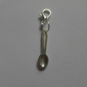 Op de afbeelding: Een zilverkleurige lepelbedel met een karabijnsluiting. De lepel heeft een gedetailleerde steel en een afgeronde kom. Deze bedel is geschikt voor het maken van sieraden of als decoratief accent.