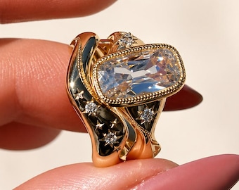 May include: A gold ring set featuring a large rectangular, clear gemstone. The ring has a black enamel design with gold stars and small diamonds. The ring is held between two fingers.