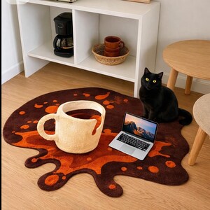 May include: A coffee-themed rug with a large, cream-colored coffee cup spilling brown and orange liquid. A black cat with yellow eyes sits near a laptop on the rug. A coffee maker and cups are on a shelf in the background.