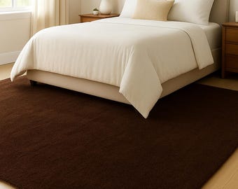 May include: A bedroom with a bed featuring a cream-coloured headboard, bedding, and a brown rug. The rug covers a large portion of the floor. A lamp and bedside table are visible on the right. A window with curtains is on the left.