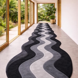Könnte beinhalten: Ein langer, wellenförmiger Teppich in Grau- und Schwarztönen. Das Design des Teppichs zeigt eine Reihe von fließenden, geschwungenen Streifen, die einen modernen Look erzeugen. Der Teppich liegt in einem Flur mit großen Fenstern und Blick ins Grüne. Der Teppich ist ca. 500 cm lang.