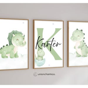 May include: Three framed art prints with dinosaur illustrations. The prints show a triceratops, a baby dinosaur hatching, and a standing dinosaur. The middle print has the name "Karter" and a large letter "K". The prints are in a nursery theme.