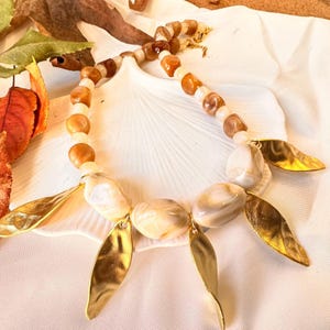 Colar de contas acrílicas com pingentes de folhas banhados a ouro em tons de âmbar marrom.