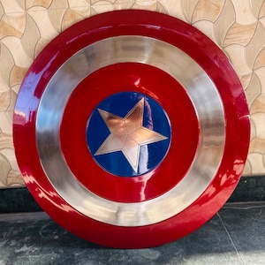 May include: A round shield with a red outer ring, a silver middle ring, and a blue center. A silver star is in the center of the blue circle. The shield has a glossy finish.