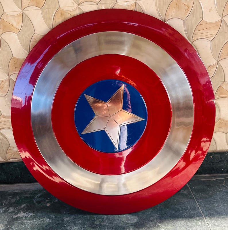 May include: A round shield with a red outer ring, a silver middle ring, and a blue center. A silver star is in the center of the blue circle. The shield has a glossy finish.