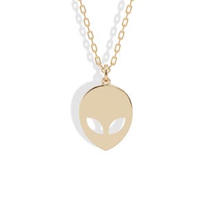 Può includere: Una collana color oro con un ciondolo a forma di testa di alieno. Il ciondolo ha due ritagli a forma di mandorla per gli occhi. La catena è a maglie sottili, su sfondo bianco.