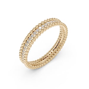 Op de afbeelding: Een geelgouden ring met een centrale rij kleine, ronde, heldere edelstenen, geflankeerd door twee rijen gepolijste, bolvormige gouden kralen die aan beide zijden van het cirkelvormige sieraad een getextureerde rand creëren.