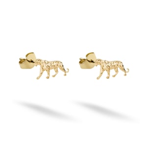 Puede incluir: Un par de pendientes dorados. Cada pendiente presenta un diseño de leopardo detallado y texturizado. Los pendientes están sobre un fondo blanco, con una sombra debajo.