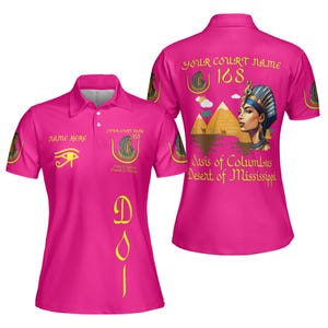 Peut inclure: Un polo rose vif à manches courtes. Le t-shirt présente du texte et des graphiques dorés, dont un symbole d'œil, une pyramide et les mots "NAME HERE" et "YOUR COURT NAME 168". Le dos du t-shirt a un graphisme de femme égyptienne.
