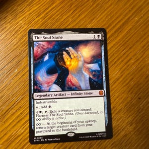 May include: A Magic: The Gathering trading card titled The Soul Stone, featuring a cosmic illustration of hands holding a glowing orange orb. The card text includes Legendary Artifact, Infinity Stone, Indestructible, and game mechanics.