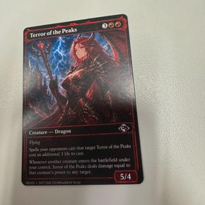 May include: A Magic: The Gathering trading card titled Terror of the Peaks featuring a red-haired character in dark armour holding a staff against a lightning-filled sky. The card text includes creature type Dragon, ability Flying, and power/toughness 5/4.