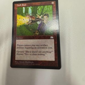 May include: A Magic: The Gathering trading card titled Null Rod with a red border and a cost of 2. The artwork depicts a figure holding a metallic device emitting yellow sparks. The text reads: Players cannot play any artifact abilities requiring an activation cost.