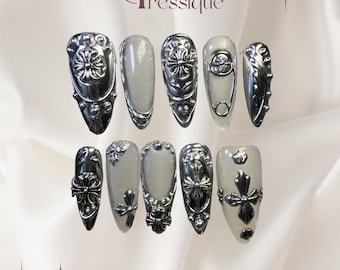 Uñas postizas estilo gótico stiletto: cruces cromadas plateadas, detalles metálicos.