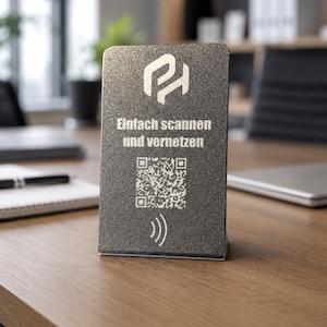 Op de afbeelding: Een rechthoekig donkergrijs getextureerd bord met een wit logo bovenaan, de Duitse tekst "Einfach scannen und vernetzen" in het midden, een QR-code onder de tekst en een wit draadloos signaalpictogram onderaan het display.
