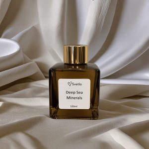 Puede incluir: Botella cuadrada de vidrio marrón con tapón dorado. La etiqueta blanca tiene el texto "Svetlo Deep Sea Minerals 100ml". La botella está sobre una tela crema drapeada. Contiene 100 ml.