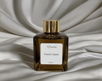 Può includere: Una bottiglia di vetro marrone con tappo dorato, etichettata "Fresh Linen" con il marchio "Svetlo". La bottiglia contiene 100 ml di liquido. La bottiglia, di forma quadrata, è appoggiata su una superficie bianca e setosa.