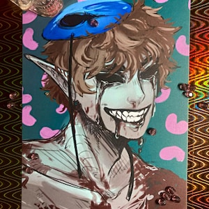 May include: A rectangular art print featuring a stylized illustration of a character with brown hair, pointed ears, and a wide, toothy grin. The character wears a bright blue mask on their head and has dark liquid dripping from their eyes and mouth.