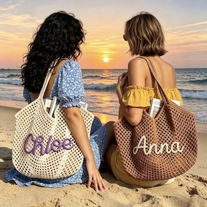 Puede incluir: Dos bolsos tote de tejido abierto con nombres personalizados est&aacute;n en una playa de arena. Uno es de color crema con el nombre "Chloe" en morado, y el otro es marr&oacute;n con el nombre "Anna" en blanco. Las bolsas est&aacute;n llenas de objetos.