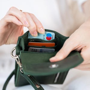 May include: A dark green leather crossbody wallet with multiple card slots. The wallet is open, revealing several credit cards. It has a silver-colored clasp and a detachable strap.