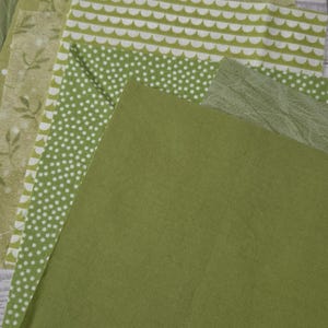 Puede incluir: Una colecci&oacute;n de cuadrados de tela en varios tonos de verde, con patrones como lunares blancos, arcos festoneados blancos e impresiones bot&aacute;nicas, junto con piezas de tela verde s&oacute;lida con texturas y superficies lisas.