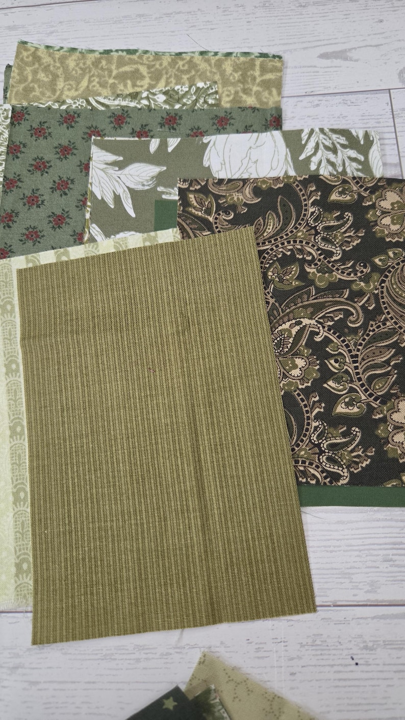 Puede incluir: Una colecci&oacute;n de muestras de tela rectangulares en varios tonos de verde, oliva y marr&oacute;n. Los patrones incluyen estampados florales, dise&ntilde;os de cachemira intrincados y una tela verde oliva s&oacute;lida con un patr&oacute;n de rayas verticales texturizadas.