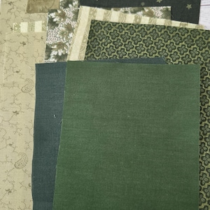 Puede incluir: Una colecci&oacute;n de retazos de tela rectangulares en varios tonos de verde y beige. Los patrones incluyen verde oscuro s&oacute;lido, un fondo verde oscuro con peque&ntilde;as estrellas, un estampado de tr&eacute;bol verde, un estampado floral beige y un patr&oacute;n de hojas beige.