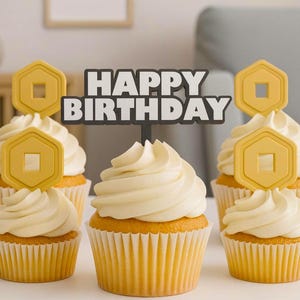 May include: Five cupcakes with white icing and yellow paper cases are arranged on a white surface. Each cupcake is topped with a yellow hexagon-shaped decoration. A sign that says "HAPPY BIRTHDAY" is placed in the centre.