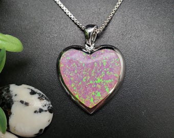 May include: A silver-toned necklace with a heart-shaped pendant. The pendant features a pink and green opal stone set in a silver bezel. The chain is a delicate box chain style.