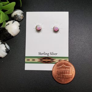 May include: A pair of sterling silver stud earrings with pink opal stones. The earrings are displayed on a white card with the words "Sterling Silver" and a Native American design. A penny is next to the card.