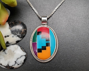 May include: Oval pendant necklace with a mosaic design. The pendant features a silver-toned rope border and a colorful mosaic of red, green, purple, black, blue, and orange. The necklace has a silver chain.