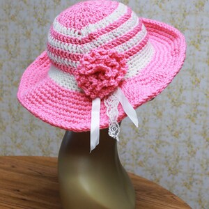 May include: A pink and white striped crochet sun hat with a pink crocheted flower and white lace trim.