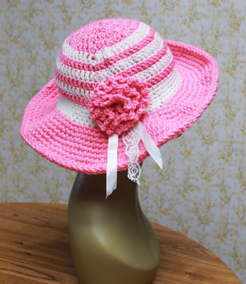 May include: A pink and white striped crochet sun hat with a pink crocheted flower and white lace trim.