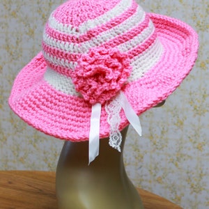 May include: A pink and white striped crochet sun hat with a pink crocheted flower and white lace trim.