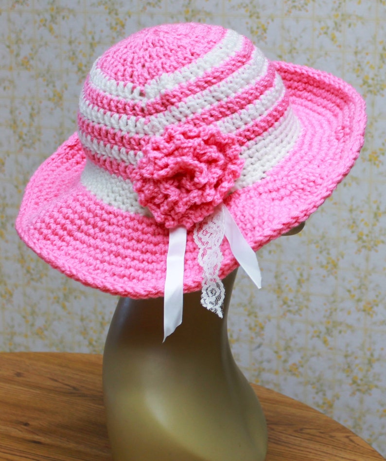 May include: A pink and white striped crochet sun hat with a pink crocheted flower and white lace trim.