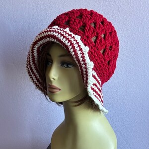 May include: A red and white crocheted hat with a wide brim. The hat has a scalloped edge and a delicate crocheted design.