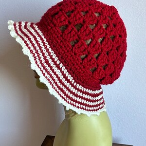 May include: Red crochet sun hat with a white and red striped brim. The hat is crocheted in a  pattern of open squares.
