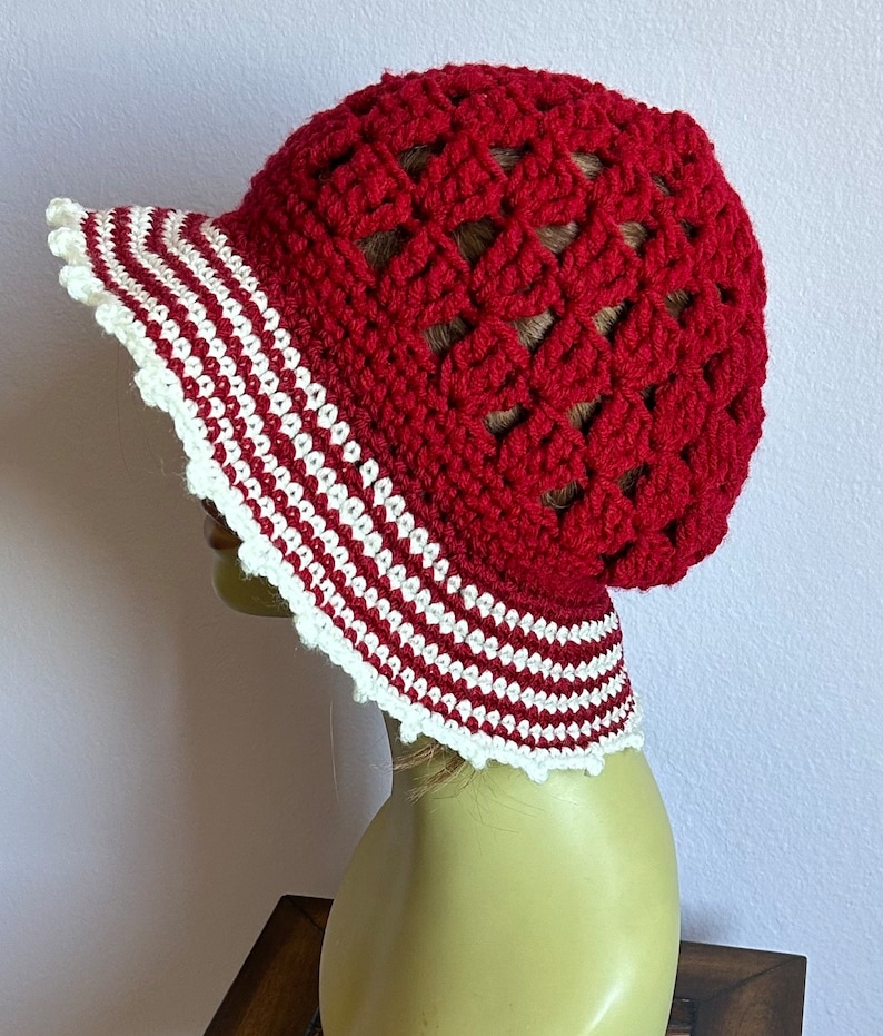 May include: Red crochet sun hat with a white and red striped brim. The hat is crocheted in a  pattern of open squares.