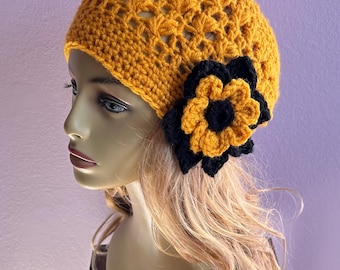 May include: Mustard yellow crochet hat with a black and yellow flower accent. The hat features an openwork design and a decorative flower on the side. This handmade hat is a stylish accessory.