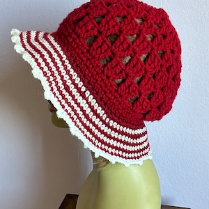 May include: Red crochet sun hat with a white and red striped brim. The hat is crocheted in a  pattern of open squares.