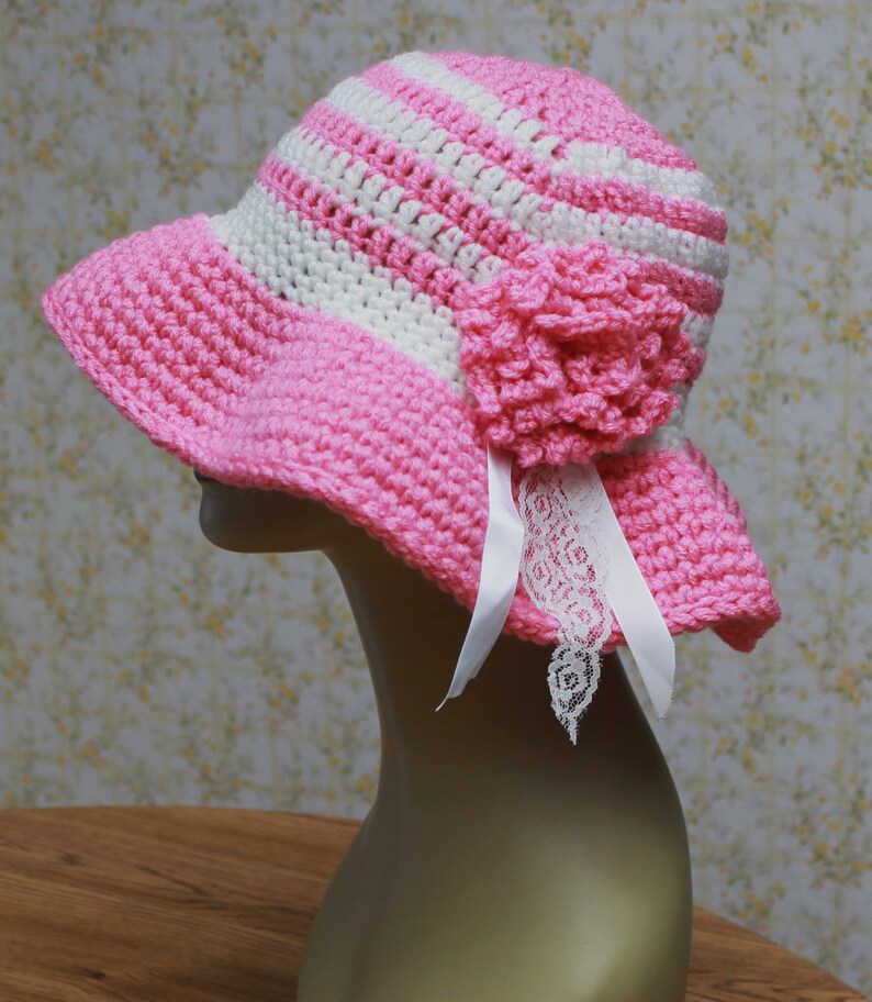 May include: A pink and white striped crochet sun hat with a pink crocheted flower and a white lace trim.