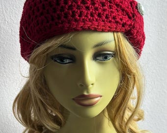 May include: A deep red, crocheted beret with a decorative silver-toned button. The hat is made of a textured yarn and has a rounded crown. The beret is displayed on a mannequin head with blonde hair.