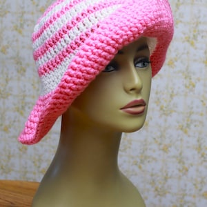 May include: A pink and white striped crochet sun hat. The hat has a wide brim and is made with a soft, textured yarn.
