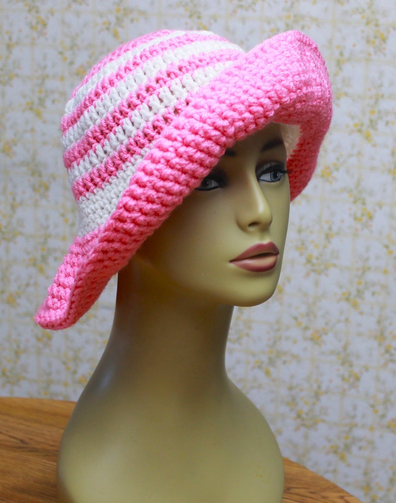May include: A pink and white striped crochet sun hat. The hat has a wide brim and is made with a soft, textured yarn.