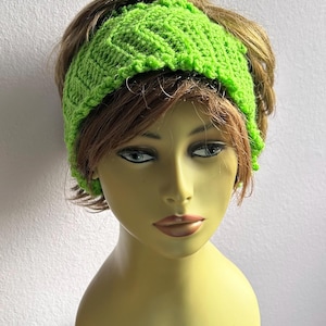 May include: A bright green knitted headband with a textured pattern. The headband is wide and covers the forehead, with a scalloped edge. The item is displayed on a mannequin head with brown hair.