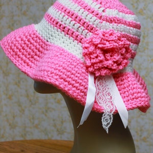 May include: A pink and white striped crochet sun hat with a pink crocheted flower and white lace trim.