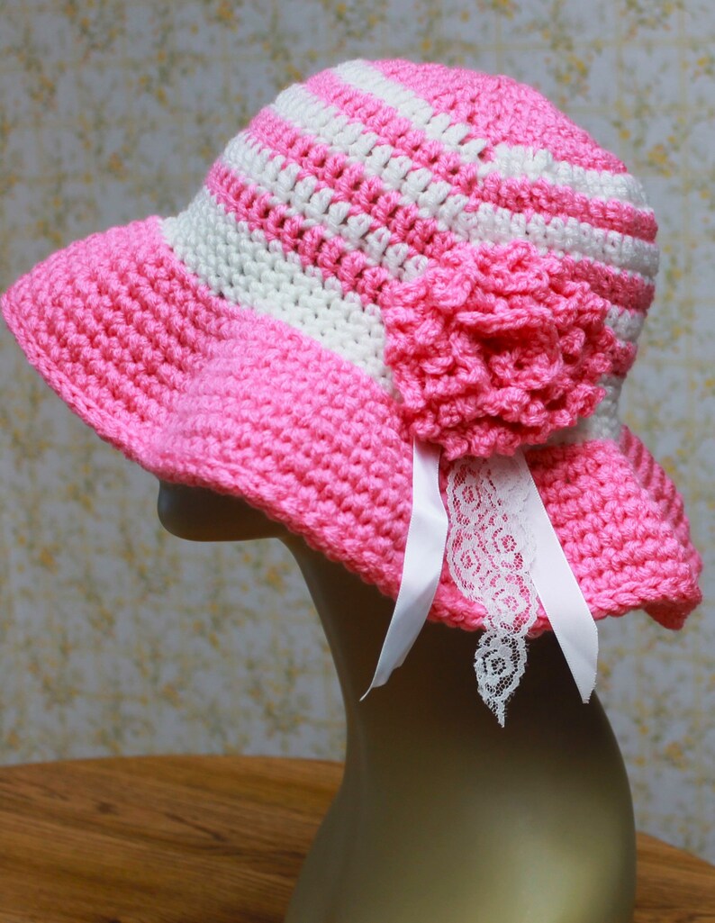 May include: A pink and white striped crochet sun hat with a pink crocheted flower and white lace trim.